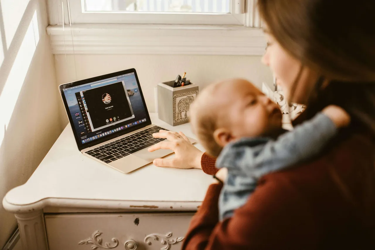 Madre lactante trabajando en una laptop mientras sostiene a su bebé, representando el equilibrio entre maternidad y vida laboral.