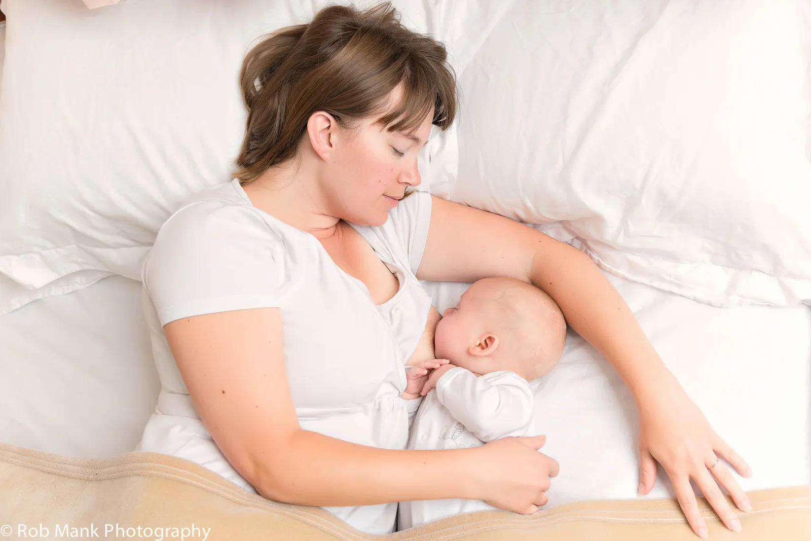 Madre amamantando de lado con bebé durmiendo cerca: “Lactancia nocturna segura y beneficios para mamá y bebé.”