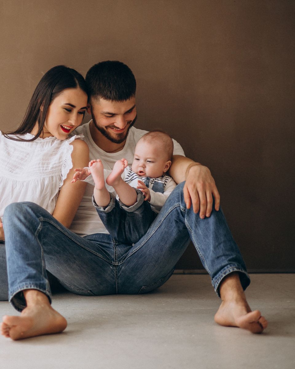 Mamá, papá y su bebé sentados juntos en el piso, sonriendo