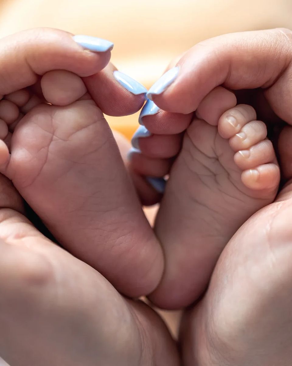 Manos de una mamá sosteniendo en forma de corazón los pies de su bebé recién nacido