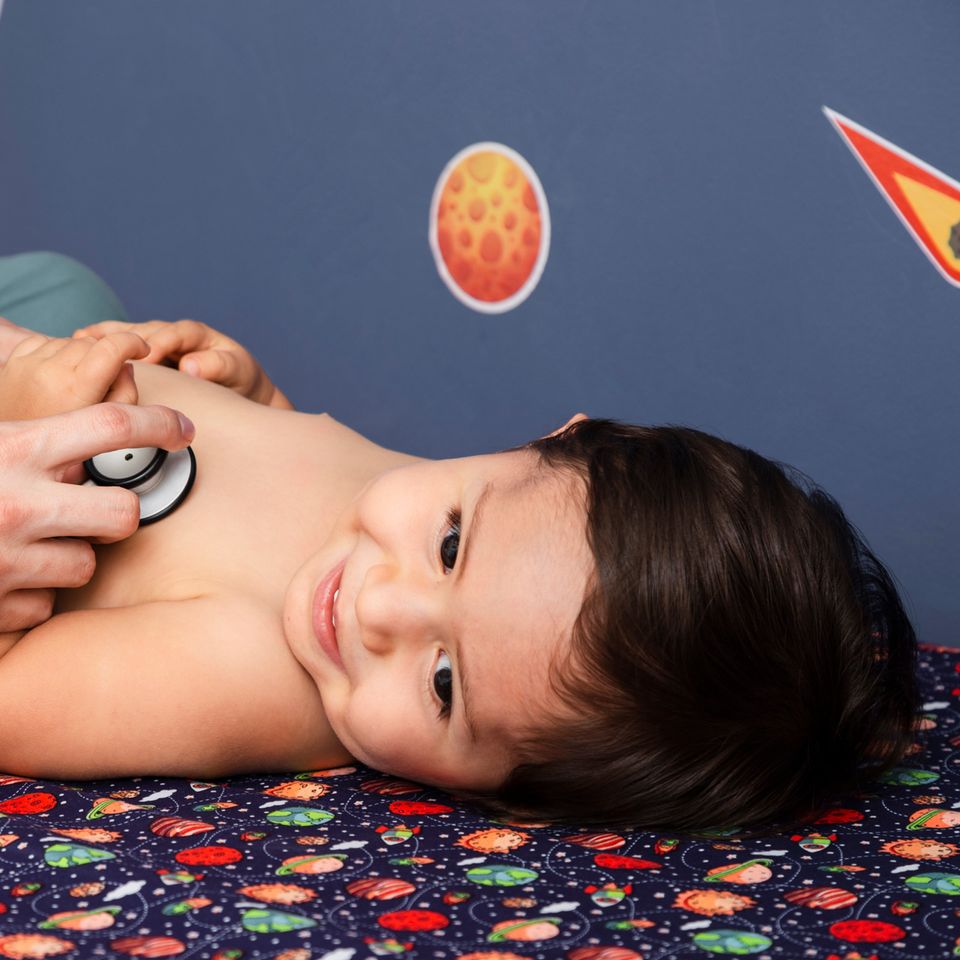 Pediatra escuchando con un estetoscopio el pecho de un niño sonriente