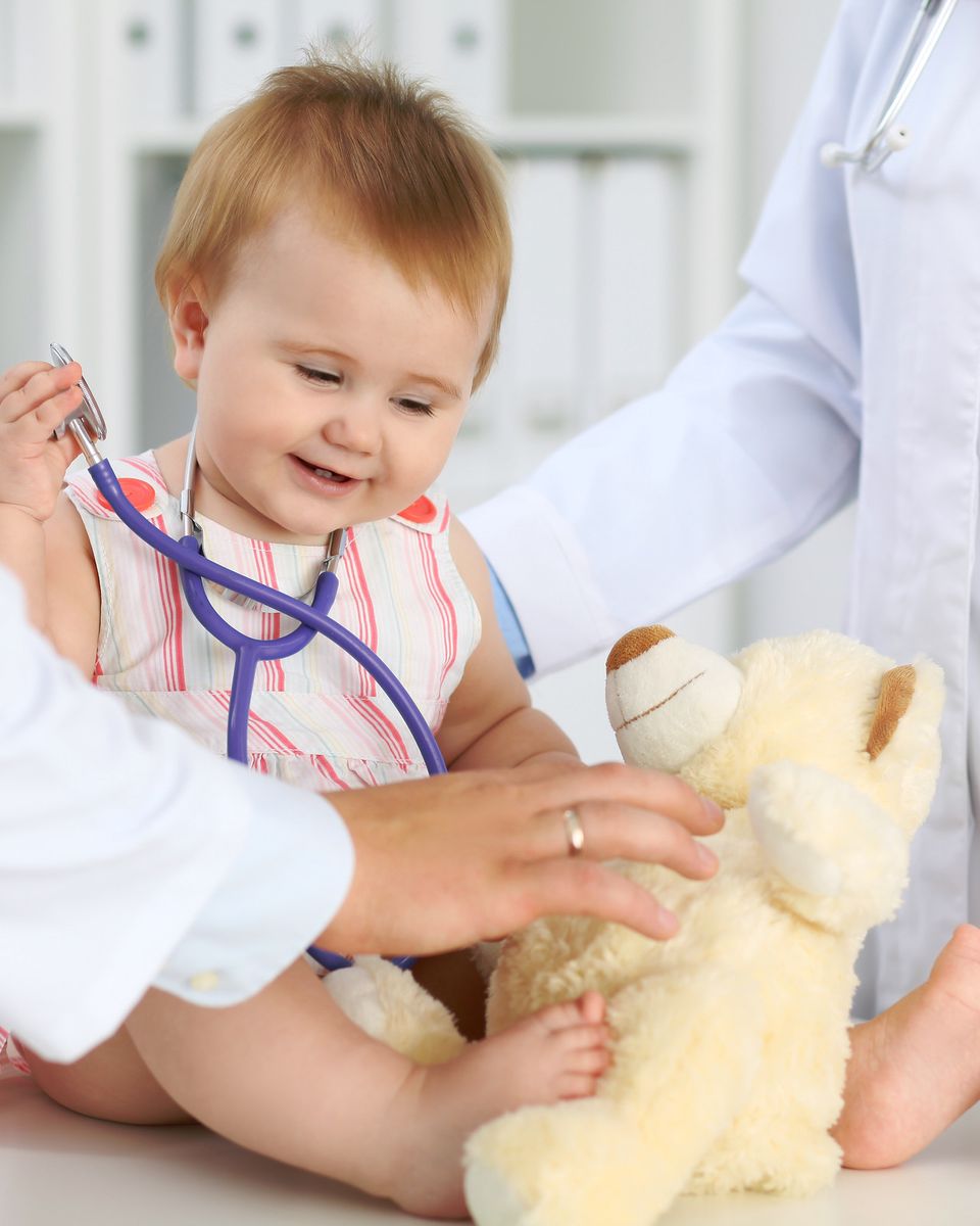 Bebé sonriente con un estetoscopio y su osito de peluche durante un chequeo médico